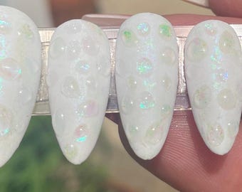 May include: Set of ten white press-on nails with iridescent glitter embedded in a clear gel. The nails are long and oval shaped.