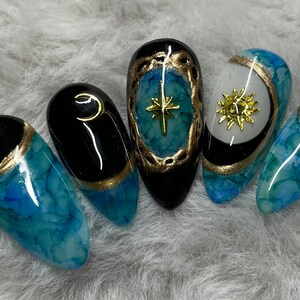 May include: Five blue and black nail tips with gold accents. Each nail tip features a different celestial design, including a crescent moon, a star, and a sun.