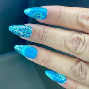 Blauwgroen en turquoise pers op de nagels met handgeschilderd abstract ontwerp. Turquoise glitter maakt deze set helemaal af. Amandel van gemiddelde lengte op foto.