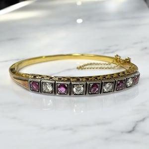 Pode incluir: Um bracelete de ouro e prata com uma fila de pedras de rubi e diamantes alternadas. O bracelete tem um detalhe de corrente delicado.