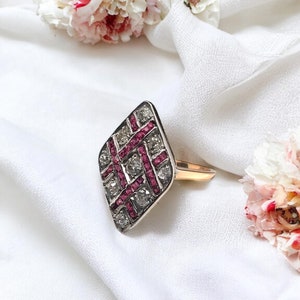 May include: A diamond and ruby ring with a geometric design. The ring is set in gold and features a square-shaped centre stone surrounded by smaller diamonds and rubies.
