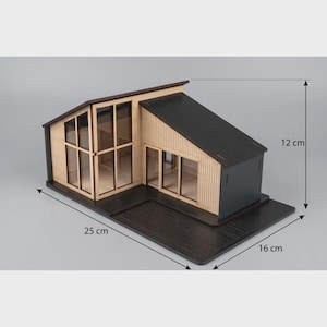 Könnte beinhalten: Ein Miniaturmodell eines modernen Hauses mit schwarzem Dach und heller Holzverkleidung, ausgestattet mit großen Glasfenstern und einem schwarzen Sockel. Das Modell misst 25 cm in der Länge, 16 cm in der Breite und 12 cm in der Höhe.