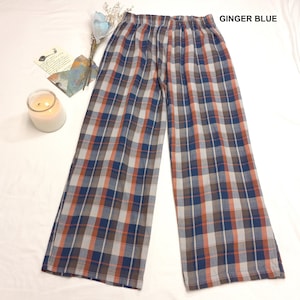 May include: Wide-leg pants in a plaid pattern with shades of blue, orange, and brown. The pants have an elastic waistband. The text "GINGER BLUE" is visible in the upper right corner. The pants are displayed on a white surface.