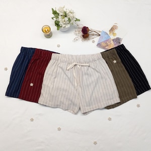 May include: A collection of five pairs of striped shorts in various colors: navy, burgundy, off-white, olive green, and black. Each pair features a drawstring waist and a small decorative embellishment.