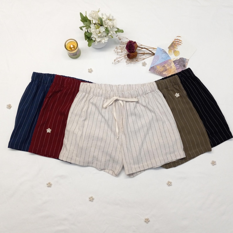 May include: A collection of five pairs of striped shorts in various colors: navy, burgundy, off-white, olive green, and black. Each pair features a drawstring waist and a small decorative embellishment.