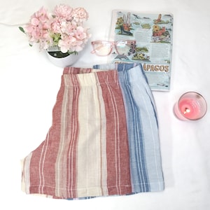 May include: A pair of striped linen shorts with a red, white, and blue color scheme. The shorts have a wide waistband and a relaxed fit.