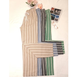 May include: Five pairs of striped pants in different colors, including beige, blue, black, and green. The pants are folded and stacked on top of each other.