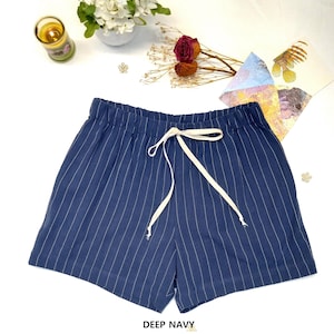 May include: Deep navy blue shorts with vertical white pinstripes. The shorts have an elastic waistband and a white drawstring. The text "DEEP NAVY" is at the bottom of the image. The shorts are casual wear.
