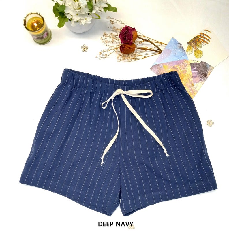 May include: Deep navy blue shorts with vertical white pinstripes. The shorts have an elastic waistband and a white drawstring. The text "DEEP NAVY" is at the bottom of the image. The shorts are casual wear.