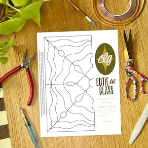 May include: A craft scene with a printed Spanish tile pattern labelled "Cutie Lil Glass." Tools include red pliers, floral scissors, a glass cutter, and copper foil tape. Green leafy plants are in the background.