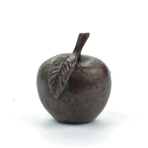 Könnte beinhalten: Eine bronzefarbene Apfelskulptur mit detailliertem Blatt und Stiel. Der Apfel hat eine glatte, abgerundete Form und ist vor einem weißen Hintergrund platziert. Die Skulptur ist wahrscheinlich aus Metall und ein dekoratives Objekt.