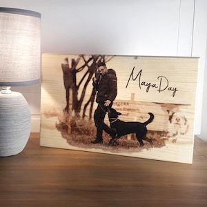 Può includere: Targa in legno con un'immagine incisa al laser di una persona che porta a spasso un cane nero. Il testo "Maya Day" è scritto in un carattere script. L'immagine è in toni seppia e la targa è esposta su una superficie di legno.