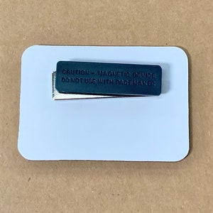 May include: A white rectangular name tag with a black magnetic strip that reads "CAUTION - MAGNETIC DEVICE DO NOT USE WITH PACEMAKER".