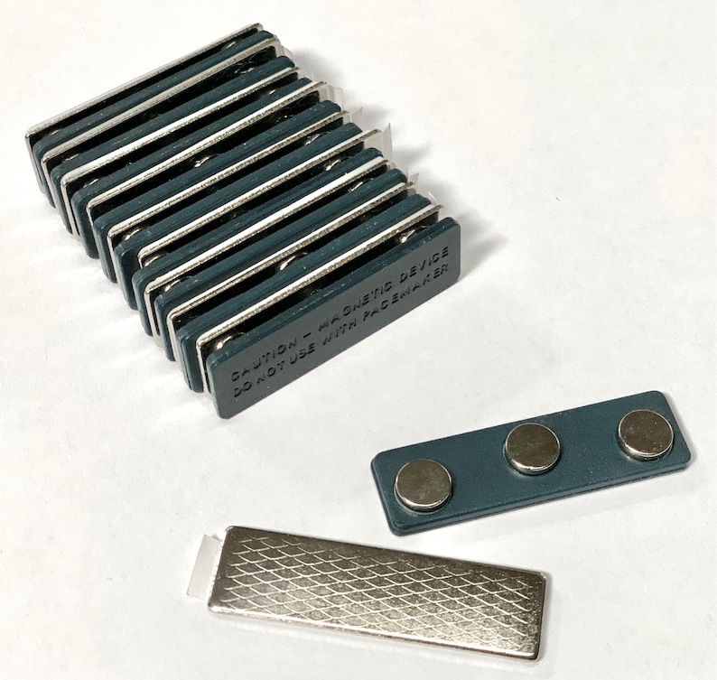 May include: A stack of 10 dark grey magnetic name tag holders with the text "CAUTION - Magnetic Device Do Not Use With Pacemaker" printed on the side. A separate name tag holder with three magnets is also shown.