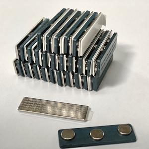 May include: A stack of 20 silver and dark blue magnetic name tags with white backing. There is also a single silver name tag and a dark blue name tag with three silver magnets.