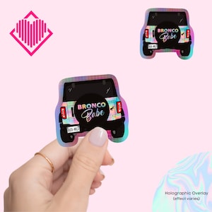 May include: Holographic sticker of a black Ford Bronco with the text "Bronco Babe" and "Buck-Wild" license plate.