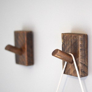 May include: Two rustic wooden wall hooks with a dark brown stain. One hook has a white cord hanging from it.