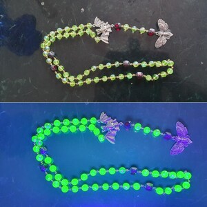 Puede incluir: Un rosario de vidrio verde con dijes de plata en forma de murciélago y mariposa. Las cuentas brillan bajo una luz negra.