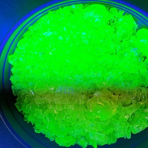 May include: A close-up of a bowl filled with bright green crystals. The crystals are translucent and have a slight shimmer to them.