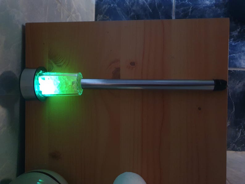 K&ouml;nnte beinhalten: Eine silberne Metallstange mit einem durchsichtigen Glaszylinder, der gr&uuml;nes Glitter enth&auml;lt. Der Zylinder wird von innen beleuchtet und erzeugt ein helles gr&uuml;nes Leuchten.