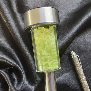 K&ouml;nnte beinhalten: Eine silberne und klare Glassolarleuchte mit einem dekorativen Design aus gr&uuml;nen Glasst&uuml;cken. Die Leuchte befindet sich auf einer schwarzen Stoffoberfl&auml;che.