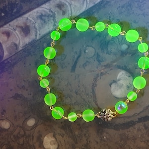 Può includere: Una collana di perline di vetro verde con una chiusura dorata e un ciondolo iridescente.