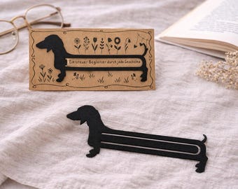 May include: Black dachshund dog bookmark with the text "Ein treuer Begleiter durch jede Geschichte" on a brown card with floral illustrations. A second black dachshund bookmark is also visible.
