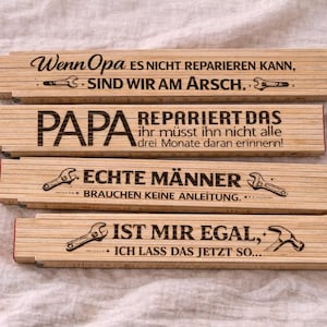 Op de afbeelding: Vier houten vouwlinialen met zwarte tekst en illustraties. De linialen bevatten zinnen als "Als opa het niet kan repareren, zijn we de klos" en "Papa repareert het". De linialen zijn lichtbruin met rode randen.