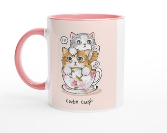 May include: A white ceramic mug with a pink handle and rim, featuring a graphic of a ginger cat and a grey tabby cat sitting inside a floral teacup. The illustration includes a speech bubble with the text Hi! and the words cute cup below.