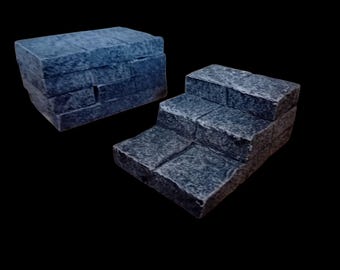 May include: Two miniature stone structures. One is a rectangular block, and the other is a set of three steps. Both are a dark gray color with a textured surface, resembling aged stone. The background is black.
