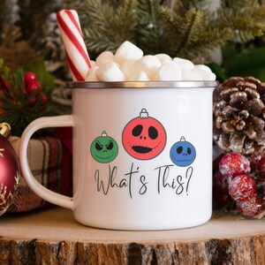 May include: White enamel mug with a red, green, and blue Christmas ornament design featuring the characters from the Nightmare Before Christmas. The text "What's This?" is printed below the ornaments. The mug is filled with marshmallows and a red and white candy cane.