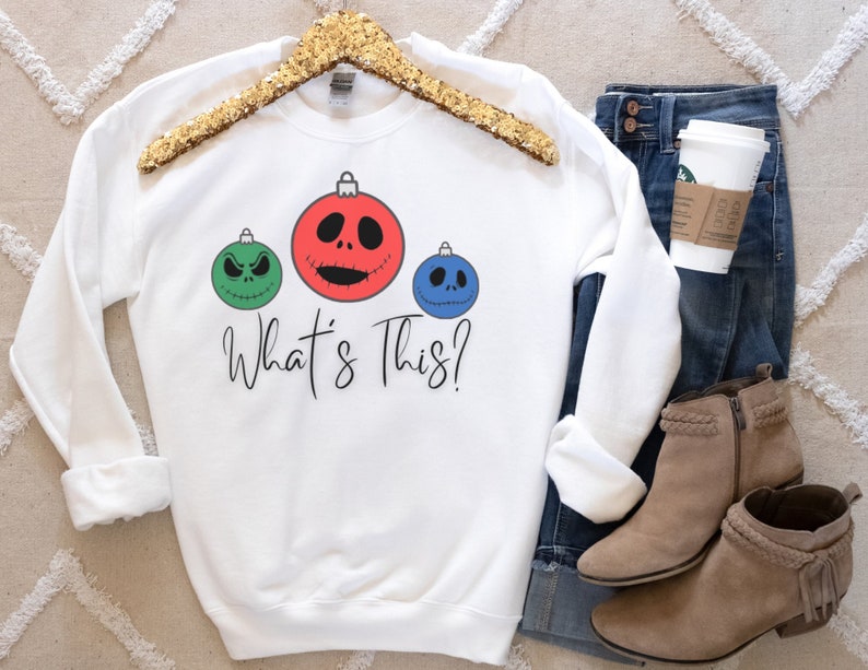 May include: White sweatshirt with a green, red, and blue Christmas ornament design featuring the characters from the Nightmare Before Christmas. The text "What's This?" is printed below the ornaments.