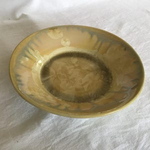 May include: A yellow ceramic bowl with a light brown glaze and a white design. The bowl has a slightly rippled edge.