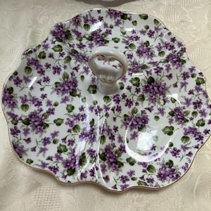 May include: A white, three-sectioned serving dish with a handle. The dish is decorated with a pattern of purple flowers and green leaves. The rim is trimmed with gold. The handle is white with a gold accent.