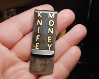 May include: A metal money clip with the words "KNIFE" and "MONEY" engraved on it in gold lettering.