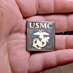 May include: A gold-colored metal pin with the words "USMC" and the Marine Corps emblem.