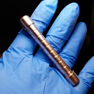 May include: A rose gold metal pen with a textured, ridged barrel. The pen is approximately 5 inches long.