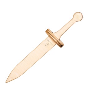 May include: A wooden toy sword with a light brown finish. The sword features a rounded handle, a crossguard, and a long, pointed blade. The text "MADE IN THE USA 2023" is printed on the blade. A small emblem is also visible.