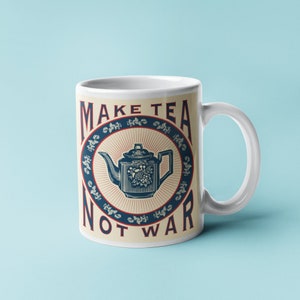 Pode incluir: Caneca de cerâmica branca com uma ilustração de bule azul e branco e o texto "Make Tea Not War" em letras vermelhas e azuis.