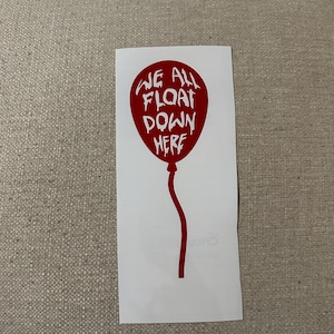 May include: A red balloon sticker with the text "WE ALL FLOAT DOWN HERE" in white. The balloon has a curved stem and is on a white background.