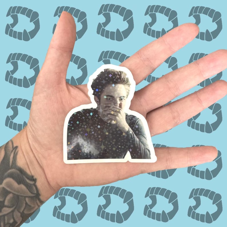 May include: A sticker featuring a portrait of a person with a hand covering their mouth, with a starry design on their shirt. The sticker is held in a hand against a light blue background with repeating vampire teeth.