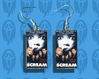 May include: A pair of silver earrings featuring miniature replicas of the Scream movie poster. Each earring has a silver hook and a rectangular charm with the Scream movie title and a scene from the film.