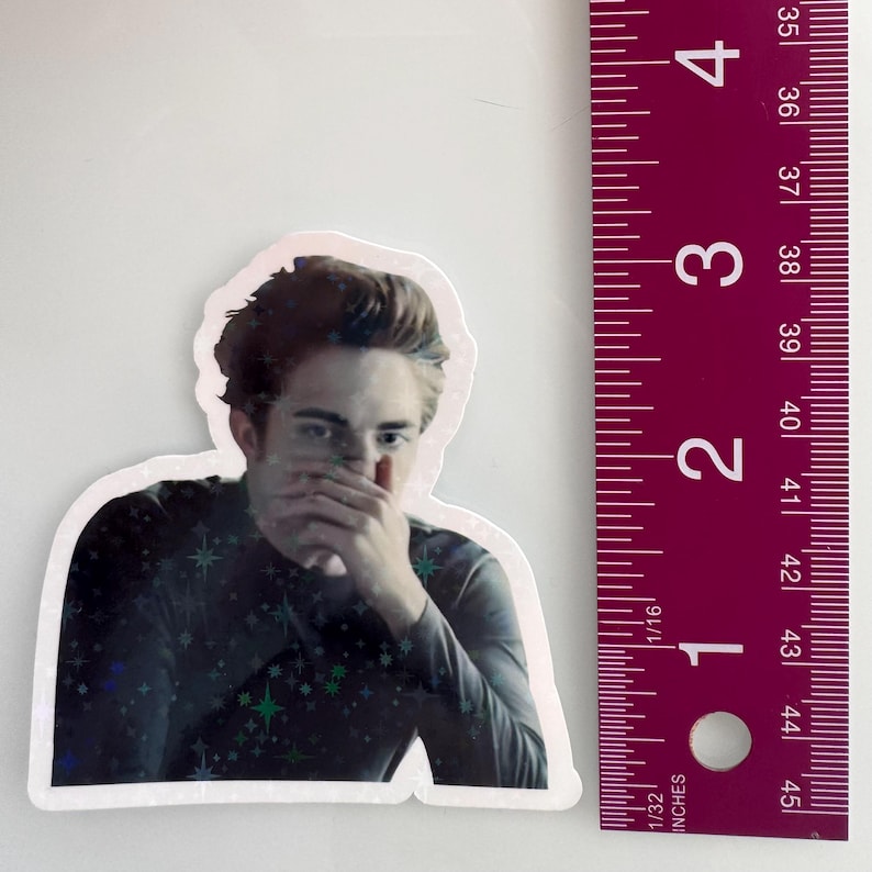 May include: A sticker featuring a portrait of a person with dark hair, covering their mouth with their hand. The sticker is approximately 3 inches tall. The person is wearing a dark long-sleeved shirt with a star pattern.