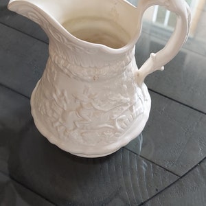 Small pitcher in the style of the W. Ridgway Co. with raised pattern of horseman on bridge and tavern with fireplace.