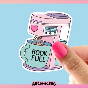 May include: A sticker featuring a pink coffee maker with a heart and the text "STRENGTH: ENTIRE BOOK." Coffee pours into a teal mug that says "BOOK FUEL." The sticker is held by a hand with pink nail polish.