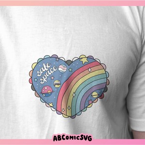 May include: A white t-shirt with a blue and rainbow heart design. The heart has stars, planets, and the text "safe space" inside.