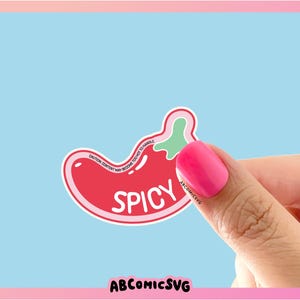 May include: A red and green chili pepper sticker with the word "Spicy" written on it. The sticker is being held by a hand with pink nail polish.
