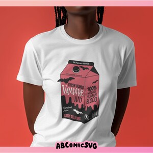 May include: White t-shirt with a graphic of a pink carton of "Fresh Blood Vampire Aid" with the text "100% Vegan Human Blood" and "Bloody Delicious".