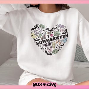 May include: White sweatshirt featuring a heart-shaped design with the text "I Summerween". The graphic is filled with summer and Halloween-themed illustrations. The sweatshirt has long sleeves and is made of a soft material.