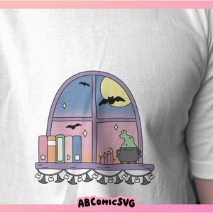 May include: White t-shirt with a cartoon window design. The illustration shows a moon, bats, books, and a cauldron with green potion. The text "ABCOMICSVG" is at the bottom of the design.
